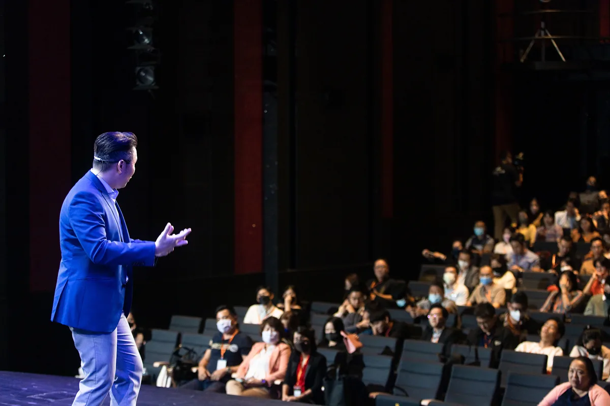 Aaron Chong speaking on stage to a seated audience